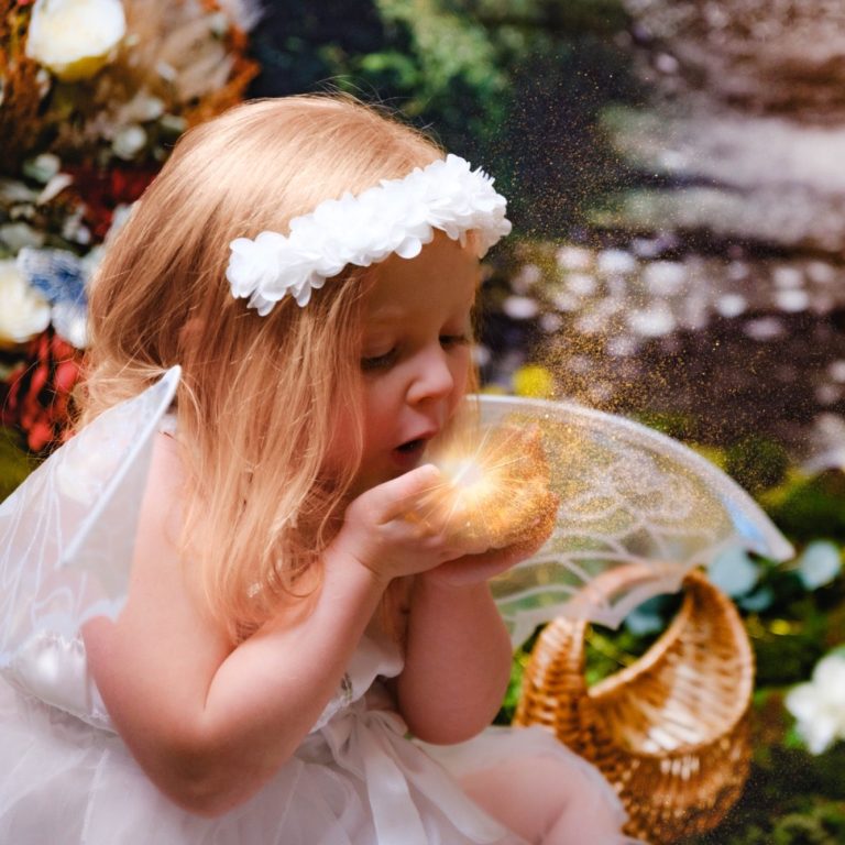 A beautiful photograph of a little girl with pale skin and blonde hair dressed as a fairy, holding an orb of light in her hands.